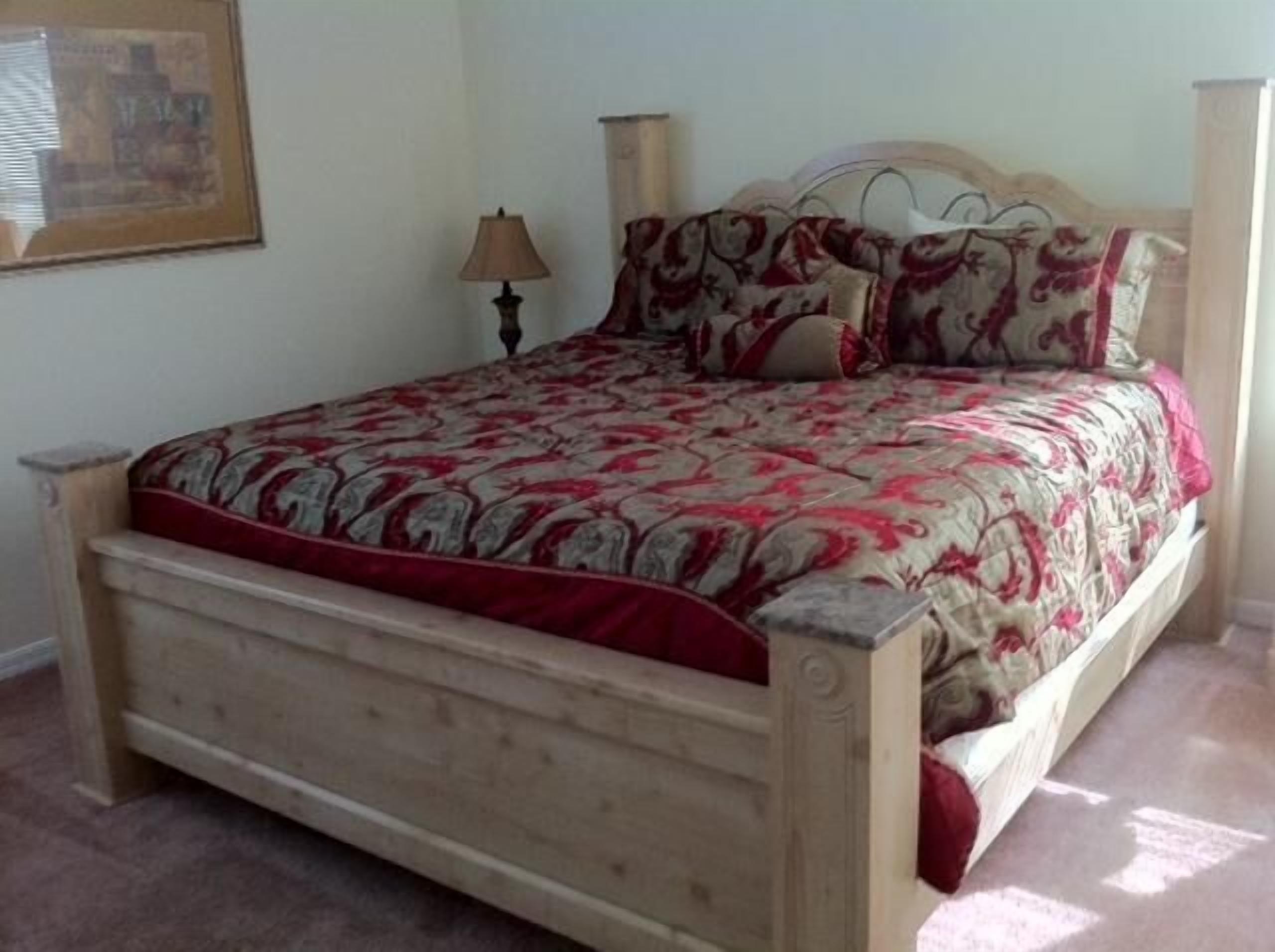 Een bed met een bedsprei met dessin, een houten hoofdbord en een nachtkastje met een lamp.