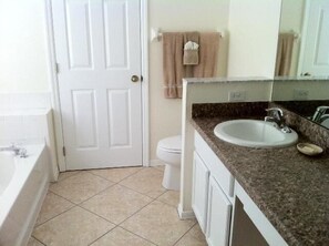 A bathroom with a white bathtub, a sink with a granite countertop, and a toilet.