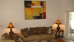 Ein Wohnzimmer mit einem beigefarbenen Sofa, zwei Lampen, einem Glastisch und einem Bild an der Wand.