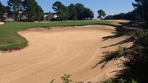 Ein Golfplatz mit Sandbunkern, grünen Fairways und Bäumen.