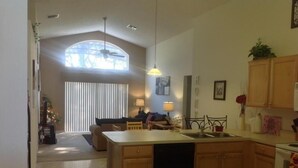 A modern kitchen with wooden cabinets, a central island, and a dining area with a sofa and chairs. - Amazing Home with Golf Course View (Haines City)