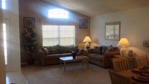 A living room with two couches, a coffee table, and a dining table with chairs. There are two lamps on the dining table and a Christmas tree in the corner. - Amazing Home with Golf Course View (Haines City)