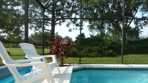 A swimming pool with white lounge chairs and a view of a green landscape. - Amazing Home with Golf Course View (Haines City)