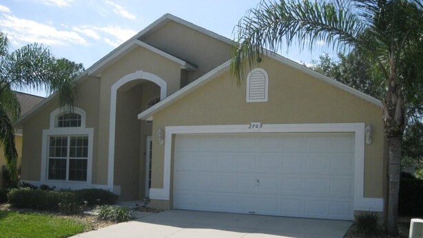 A single-story house with a garage, a front yard, and a palm tree. - Amazing Home with Golf Course View (Haines City)
