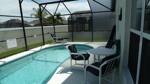 A covered outdoor swimming pool with lounge chairs and a table, surrounded by a safety fence. - Very Comfortable Villa Fully Equipped (Haines City)