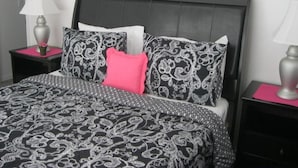 A bed with a black headboard, a patterned bedspread, and multiple pillows including a bright pink one. There are two bedside tables with lamps and a pink mat on each. - Very Comfortable Villa Fully Equipped (Haines City)