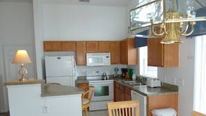 A compact kitchen with wooden cabinets, a white refrigerator, a microwave, and a sink. There is a dining area with a table and chairs. - Very Comfortable Villa Fully Equipped (Haines City)