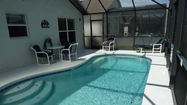 A swimming pool with clear water, surrounded by white lounge chairs and a covered patio area. - Very Comfortable Villa Fully Equipped (Haines City)