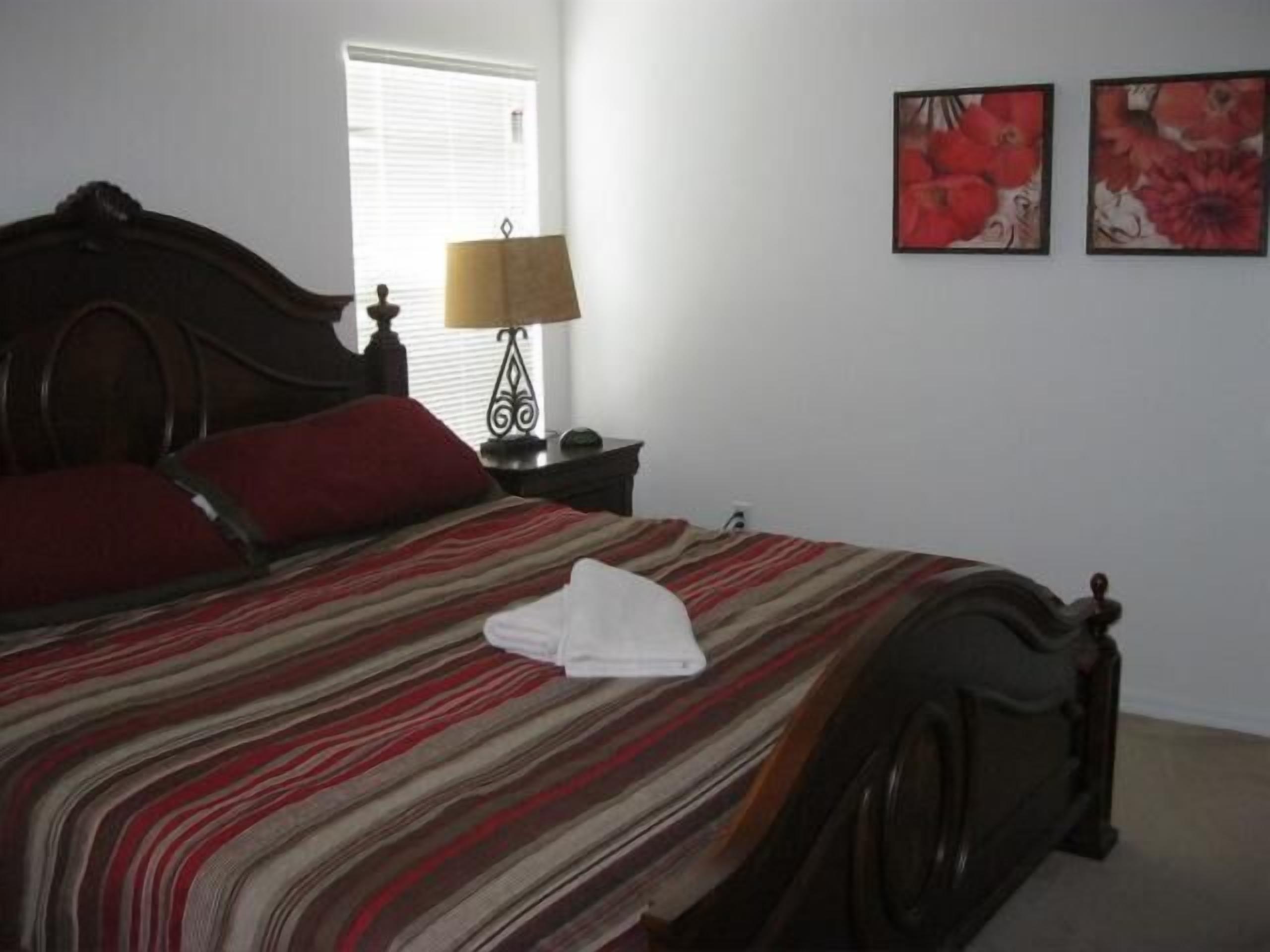 A neatly made bed with a striped bedspread, a wooden headboard, and a nightstand with a lamp.