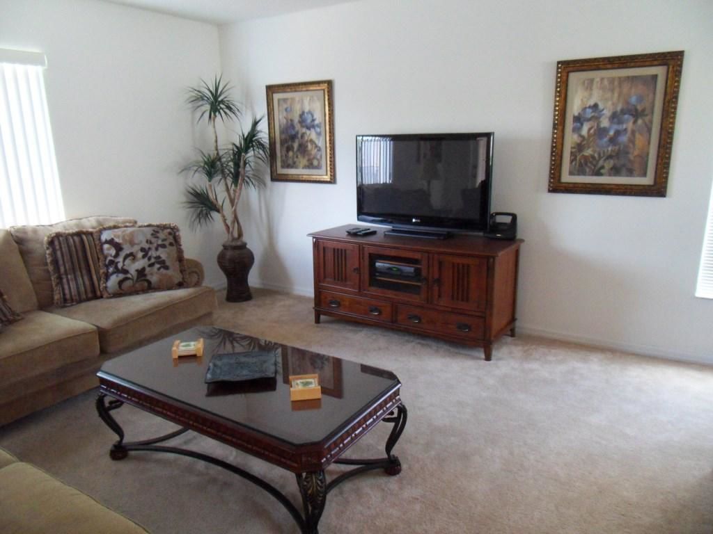 A living room with a sofa, a coffee table, a TV on a wooden cabinet, and two framed pictures on the wall.