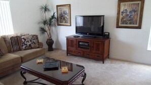 A living room with a sofa, a coffee table, a TV on a wooden cabinet, and two framed pictures on the wall. - Amazing Villa at an Exceptional Price (Haines City)