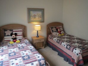 Two twin beds with matching headboards and nightstands, each with a lamp. A framed picture hangs above the beds.