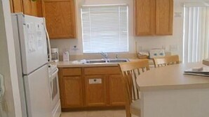 A kitchen with wooden cabinets, a white refrigerator, a sink, and a window with blinds. - Very Comfortable Villa Fully Equipped (Haines City)