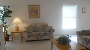 A living room with a sofa, a coffee table, a lamp, and a painting on the wall. - Very Comfortable Villa Fully Equipped (Haines City)