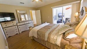 Une chambre à coucher comprenant un lit, une télévision, un ventilateur de plafond, une commode et une porte donnant sur un balcon.