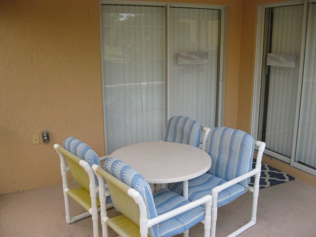 A small patio area with a round table and four chairs, each with striped cushions.