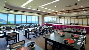 Een vergaderruimte met tafels en stoelen, grote ramen en uitzicht op zee.