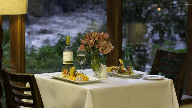 Una mesa preparada para dos, con una botella de vino, un florero y platos de comida.