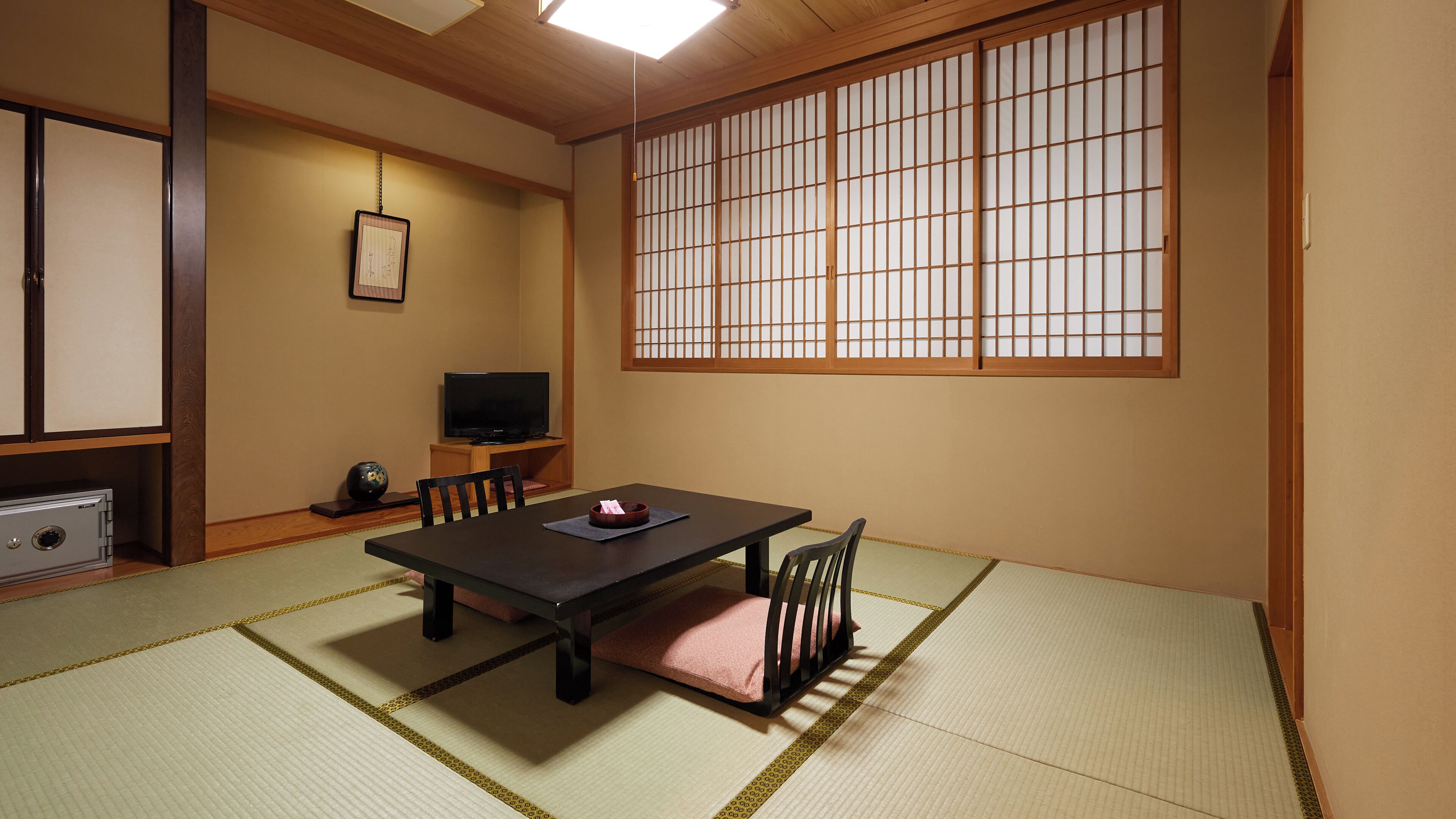 Een traditionele Japanse kamer met tatami vloerbedekking, een lage tafel, stoelen, een televisie en een shoji schuifwand.