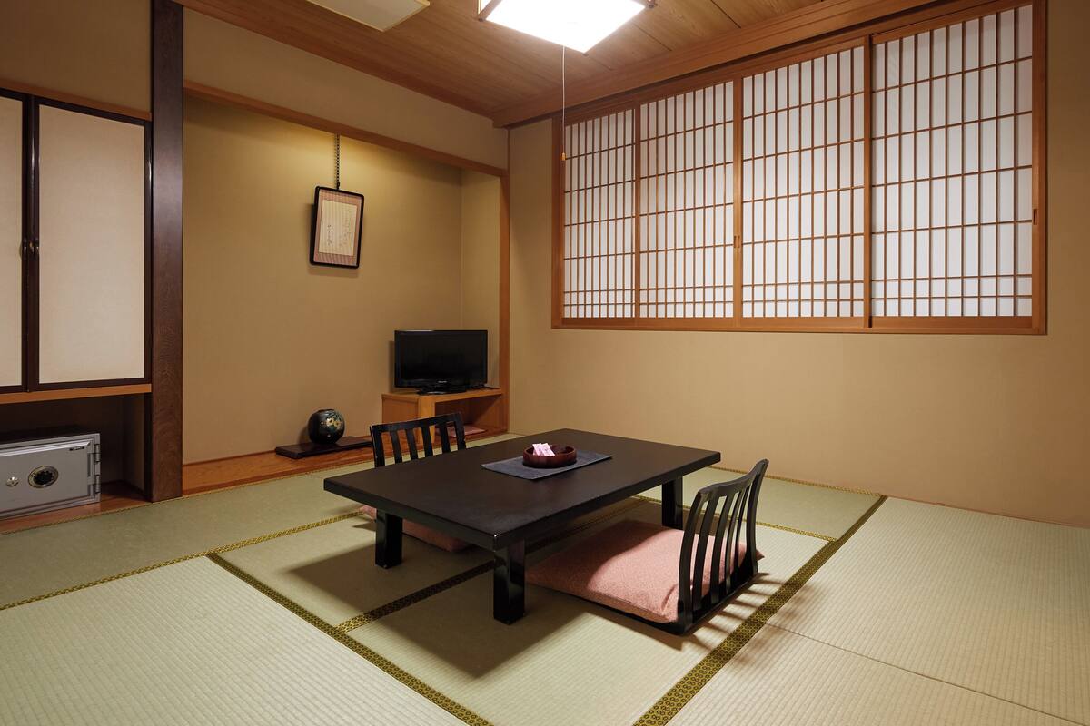 Une pièce de style japonais traditionnel, avec un sol recouvert de tatamis, une table basse, des chaises, un téléviseur et un paravent en papier de riz (shoji).