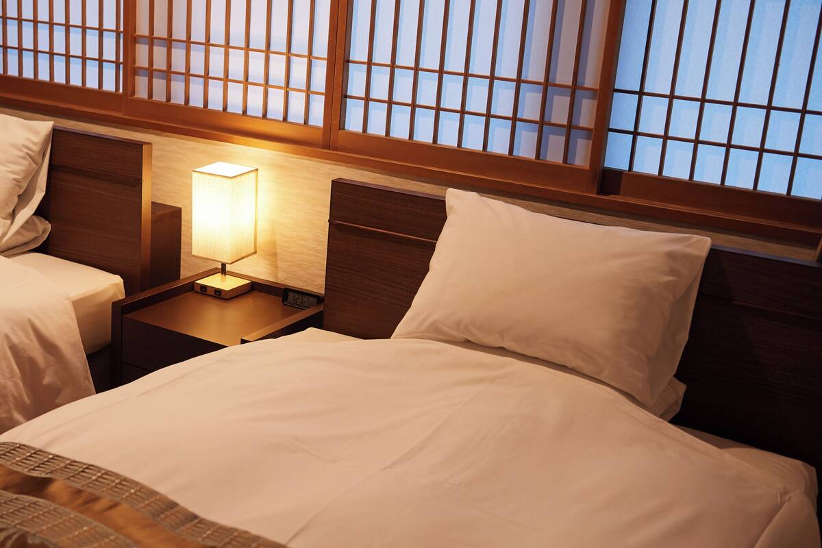 Une chambre d’hôtel avec deux lits, une table de chevet avec une lampe et une fenêtre avec des stores en bois.