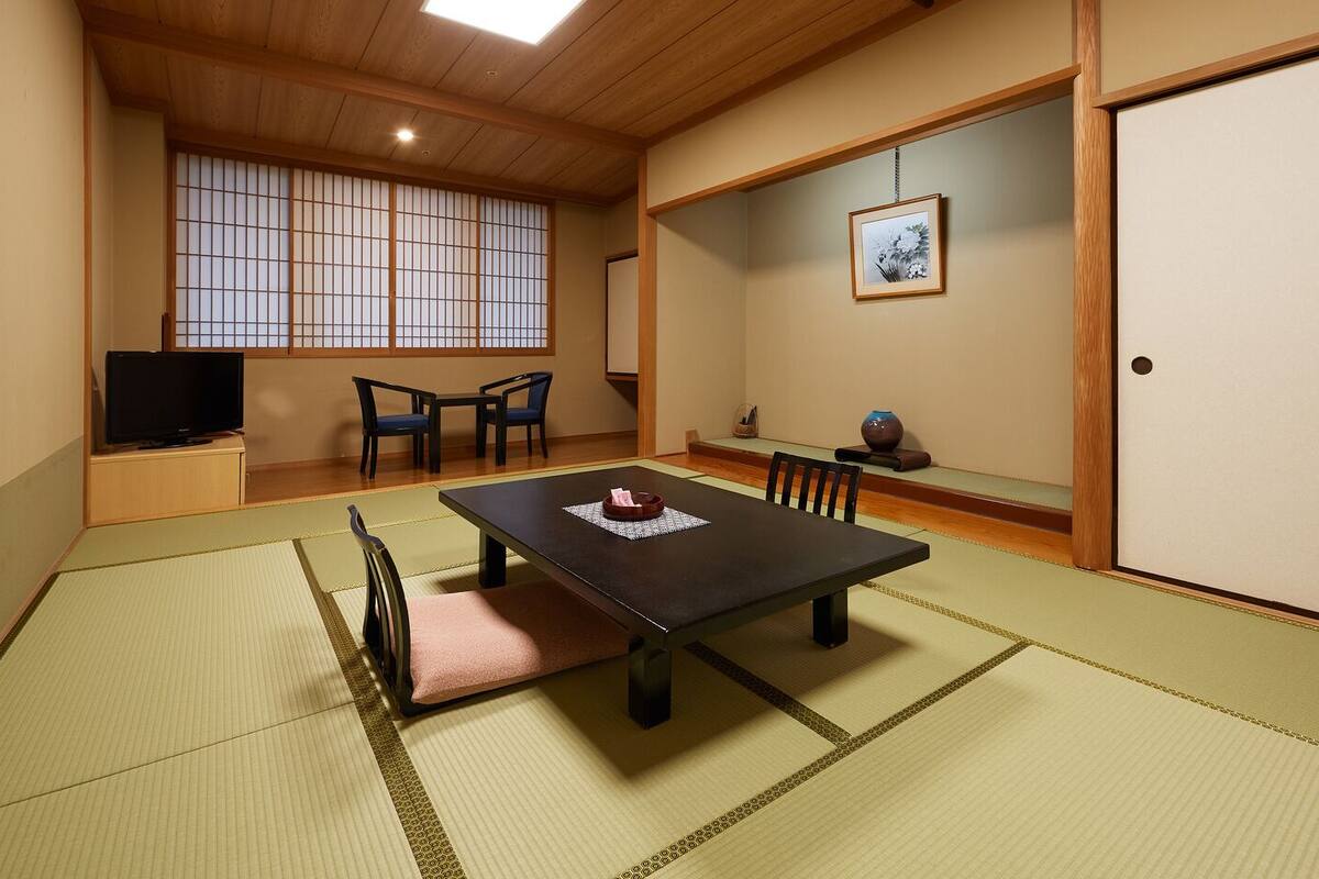 Une pièce de style japonais traditionnel, avec un sol recouvert de tatamis, une table basse, des chaises, un téléviseur et une porte coulissante.