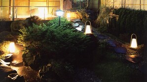 Zona de jardí ben il·luminada amb una pèrgola de fusta, un camí de pedra i diferents llums de jardí.