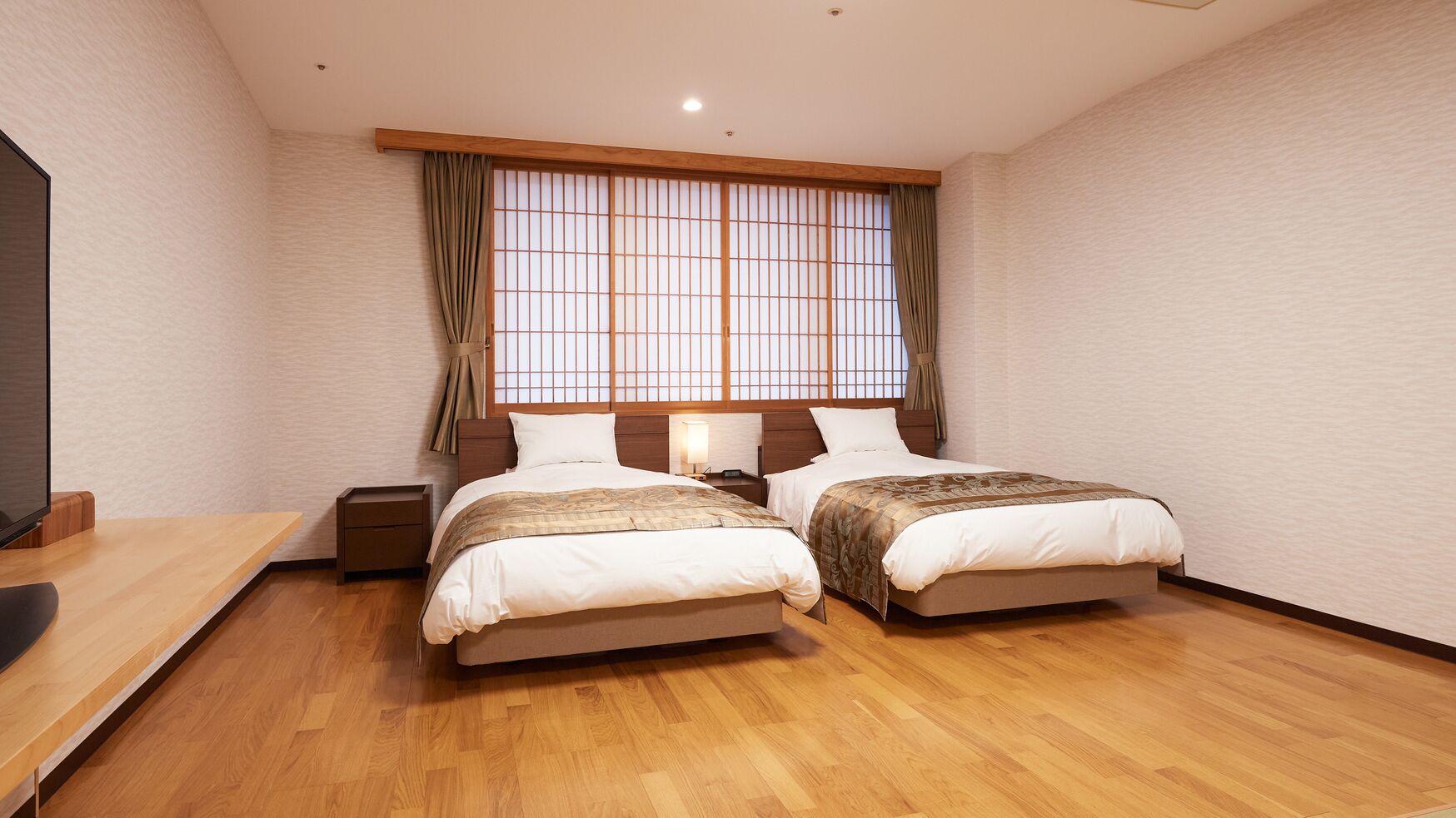 Een kamer met twee bedden, een houten vloer, een televisie en een raam met gordijnen.