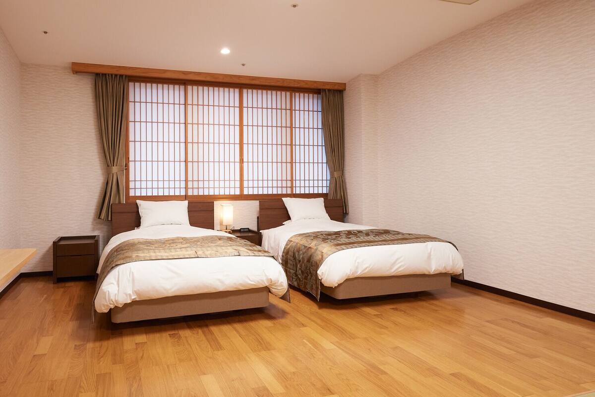 Une chambre avec deux lits, un plancher en bois, une télévision et une fenêtre avec des rideaux.