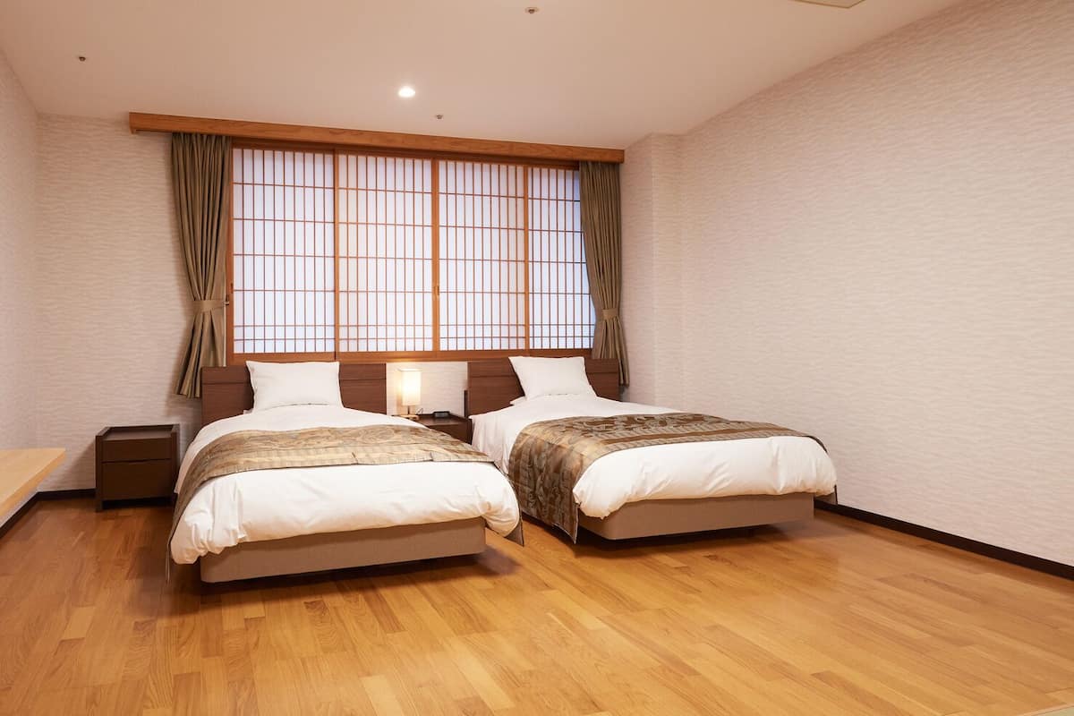 A room with two beds, a wooden floor, a TV, and a window with curtains.