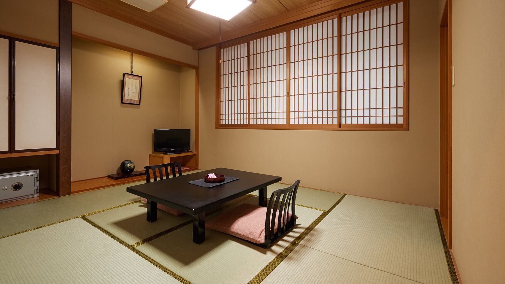 Una habitación japonesa tradicional con suelo de tatami, una mesa baja, sillas, un televisor y un divisor shoji.