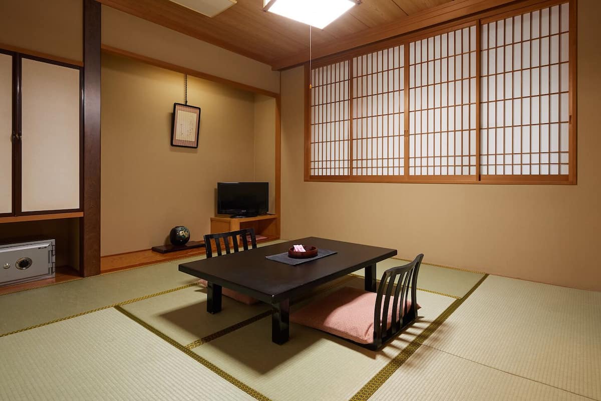 Une pièce de style japonais traditionnel, avec un sol recouvert de tatamis, une table basse, des chaises, un téléviseur et un paravent en papier.