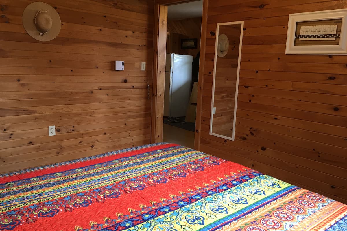 A room with wooden walls, a colorful bedspread, a mirror, and a framed quote on the wall.