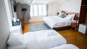 A hotel room with two beds, a desk, a lamp, a TV, and a window with curtains.
