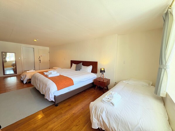 Habitación de hotel con dos camas, suelo de madera, una mesita de noche con lámpara y un espejo en la pared.