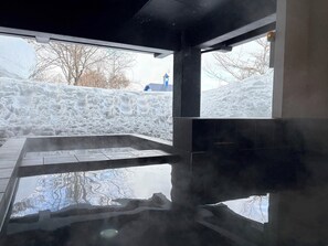 Un sauna con suelo de vidrio, vapor ascendiendo y vistas a un paisaje nevado.