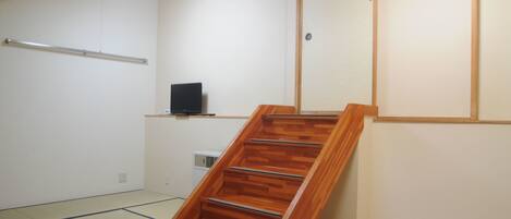 A room with a wooden staircase, a small shelf with a television, and a sliding door.