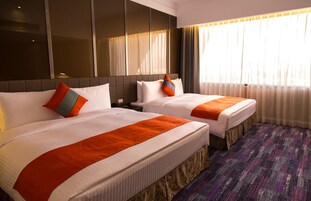 Una camera d'albergo con due letti, un'ampia finestra con tende e una moquette decorata.