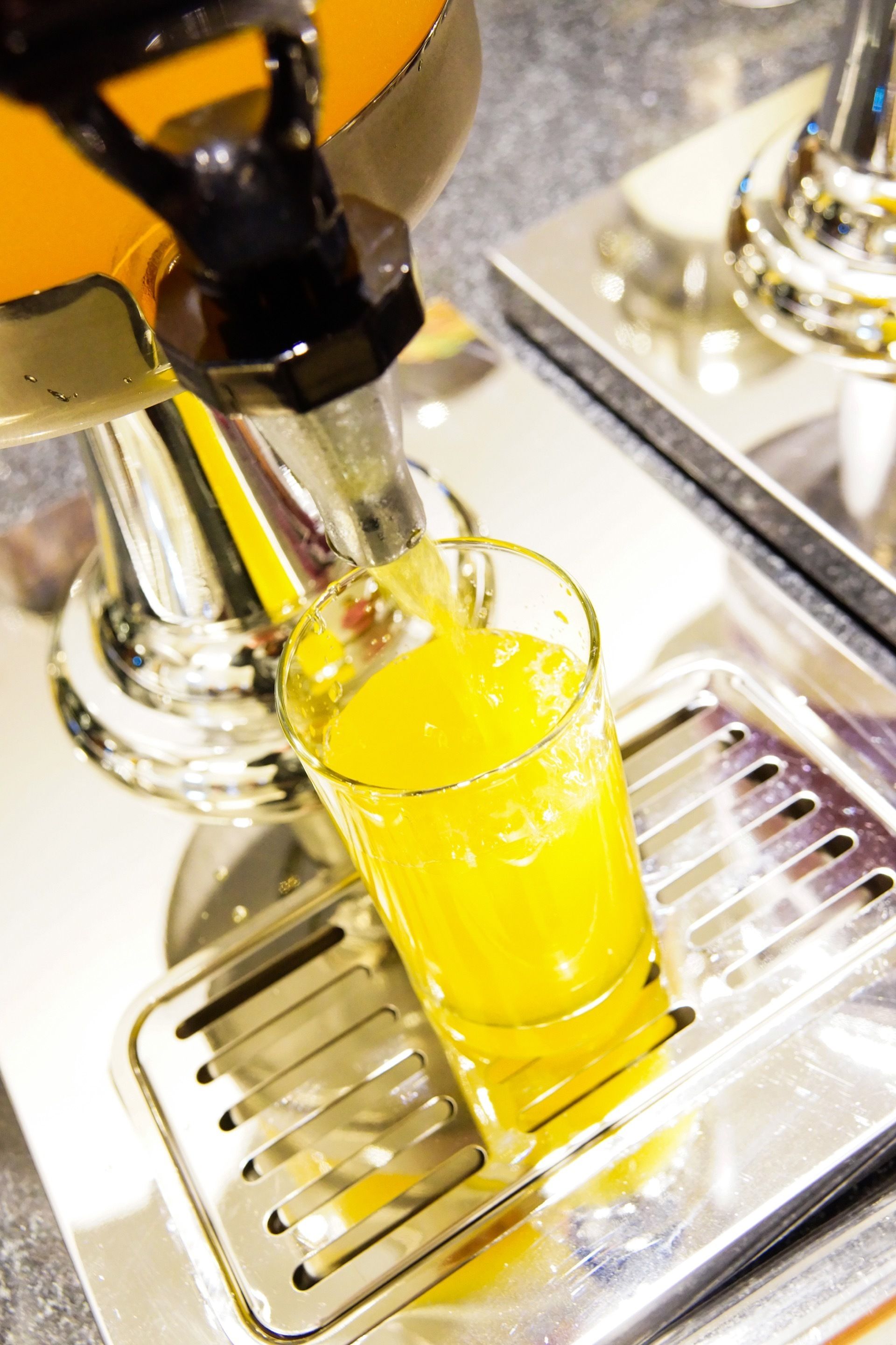 A glass of orange juice being poured from a metallic dispenser.
