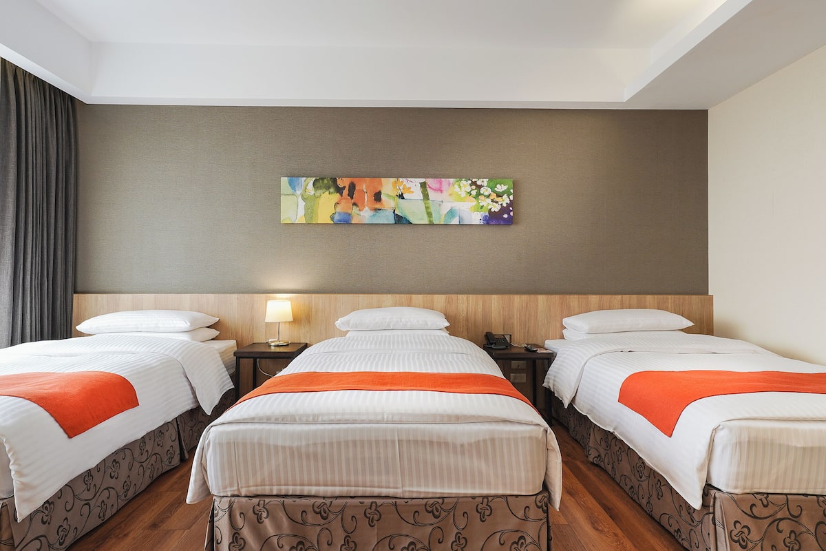 A hotel room with two beds, a painting on the wall, and a wooden floor.