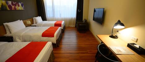 Habitación de hotel con tres camas, un escritorio, una silla, un televisor y una lámpara.
