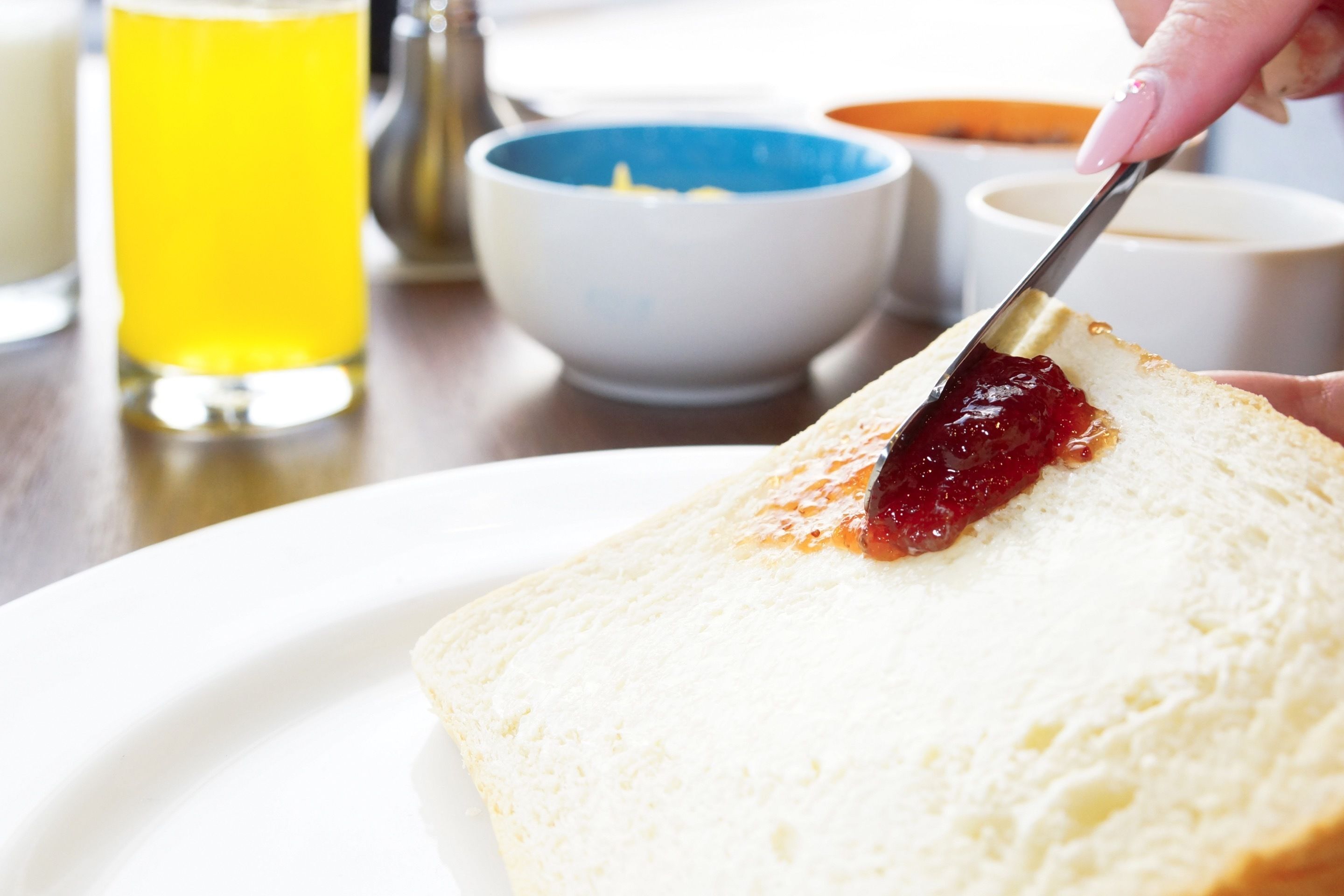 Une tranche de pain blanc avec de la confiture rouge, servie sur une assiette blanche.