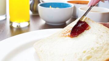 Une tranche de pain blanc avec de la confiture rouge, servie sur une assiette blanche.
