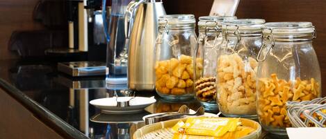 A buffet setup with various food items in jars and baskets, a coffee maker, and a tea kettle.