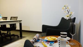 A hotel room with a dining table, a magazine, a plate with food, a cup of coffee, a glass of water, and a vase with white flowers.