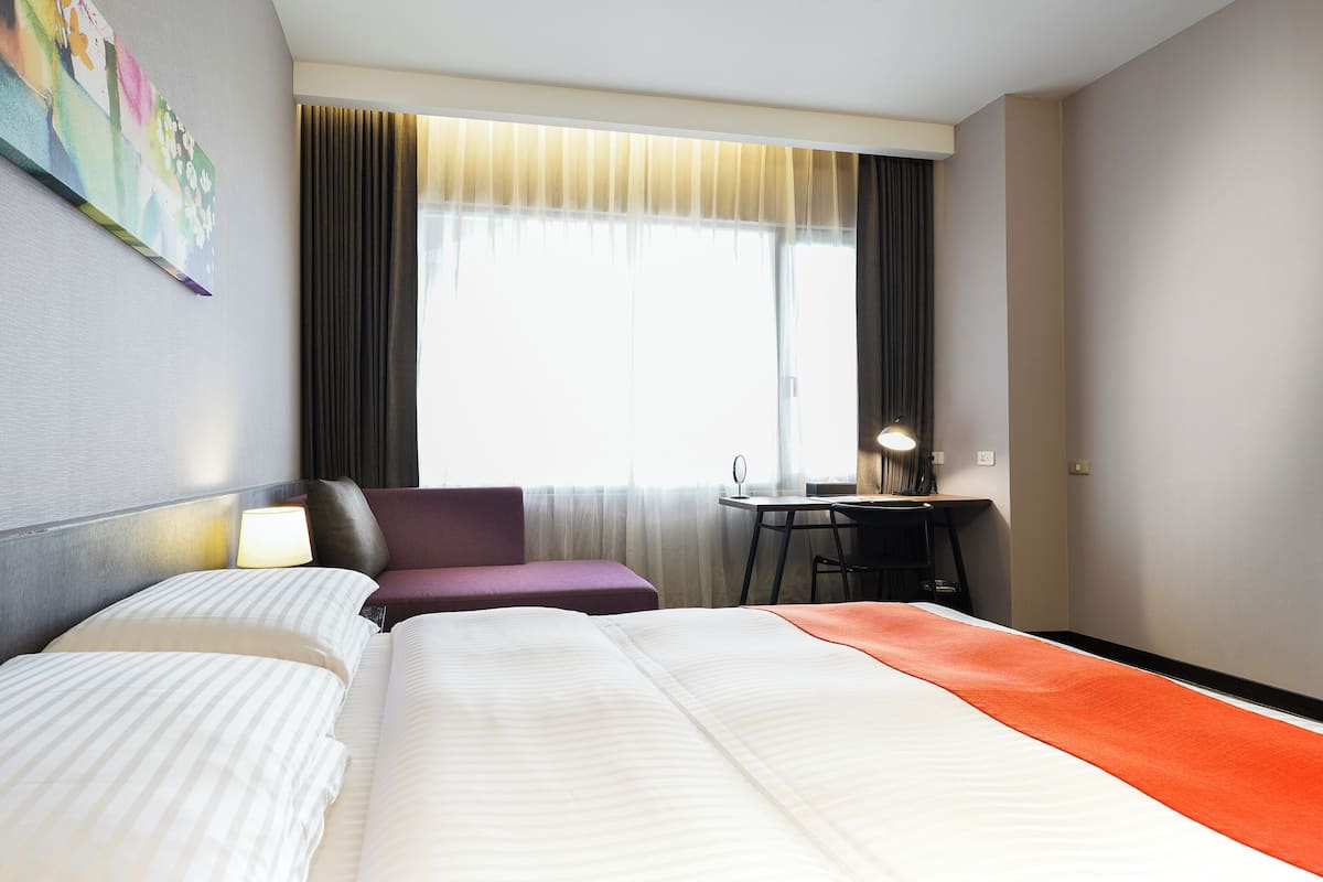 A hotel room with a large bed, a desk, a chair, and a window with curtains.