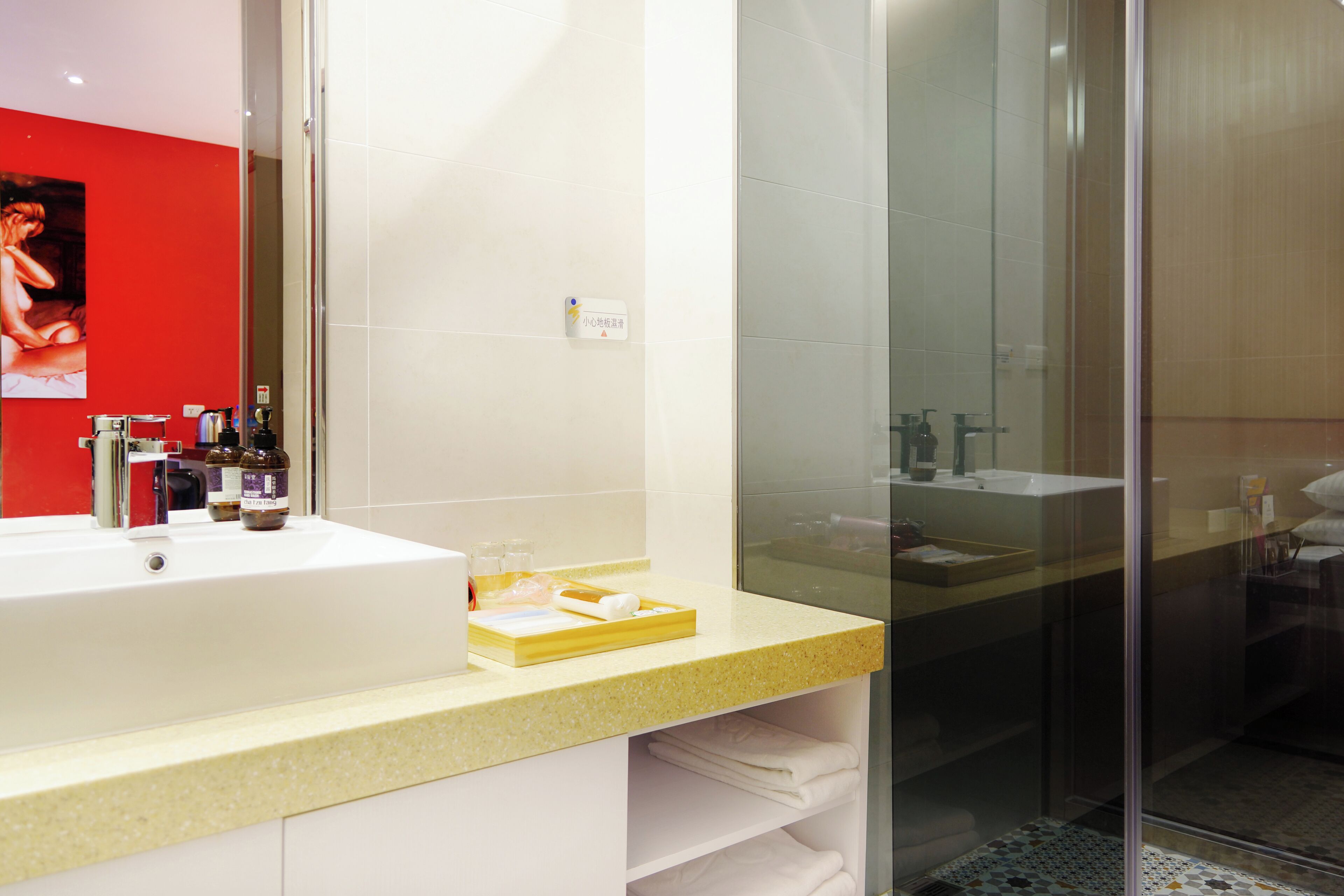 A modern bathroom with a white sink, glass shower enclosure, and a red accent wall.