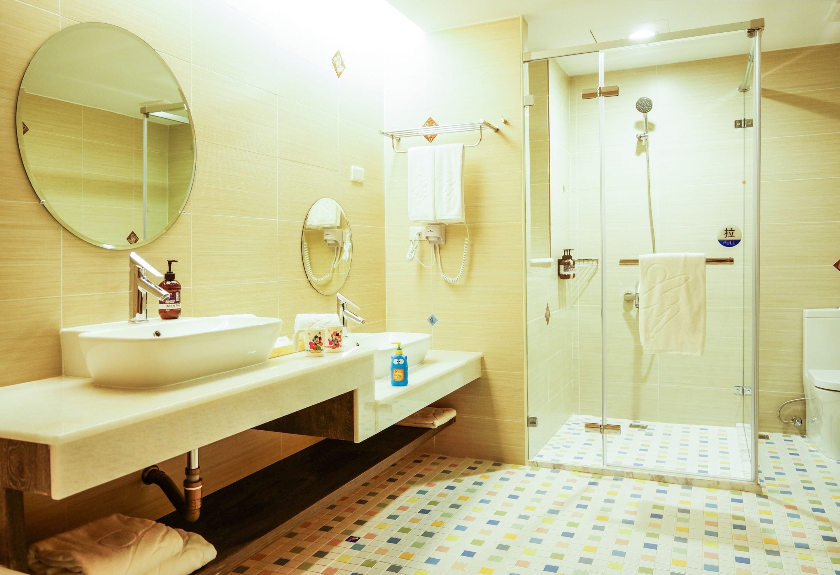 A bathroom with a large mirror, two sinks, a shower, and a tiled floor.