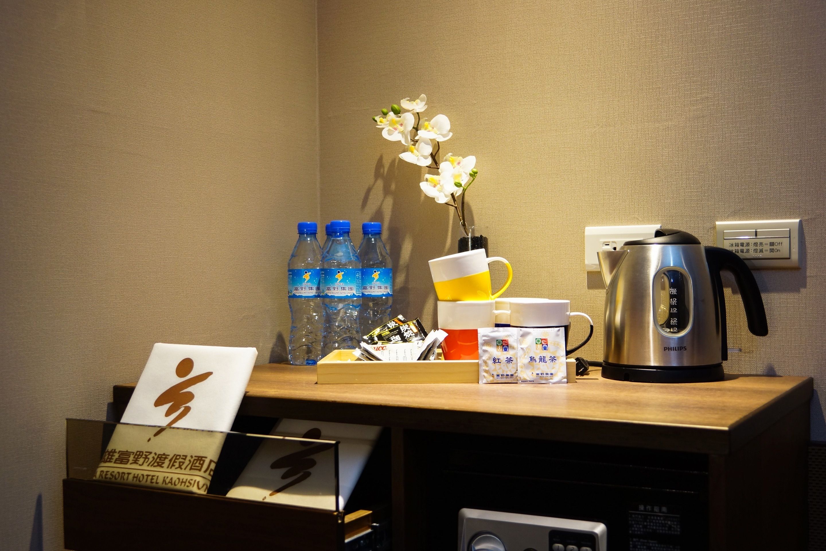 A hotel reception desk with a coffee maker, bottled water, a flower vase, and a sign with Japanese characters.