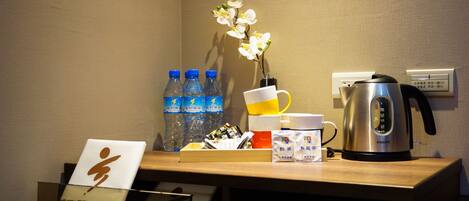 A hotel reception desk with a coffee maker, bottled water, a flower vase, and a sign with Japanese characters.